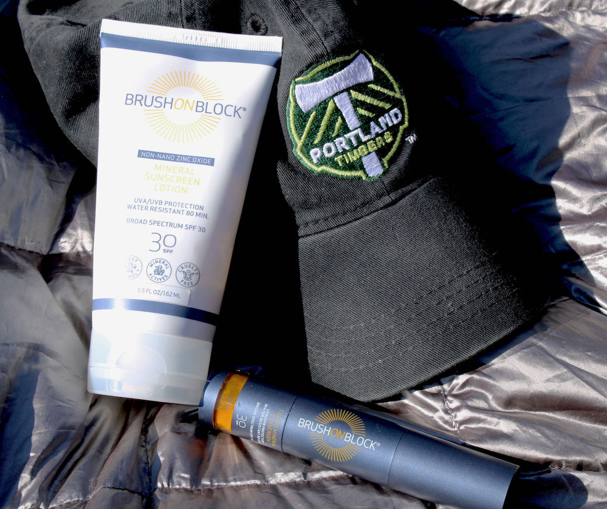 Brush On Block Mineral Powder Sunscreen SPF 30 with Brush On Block SPF 30 Mineral Sunscreen Lotion and a Portland Timbers ball cap.