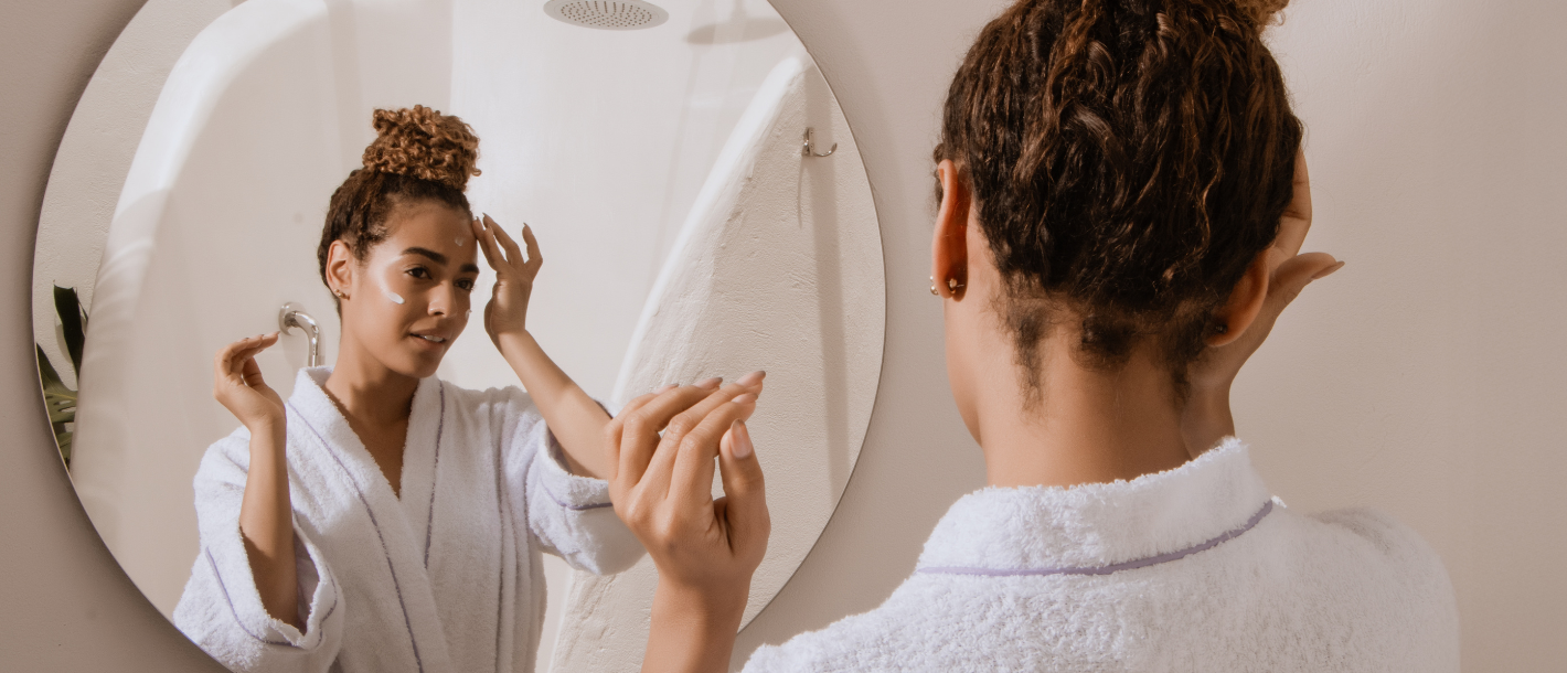 Woman applying skin care at home in mirror.