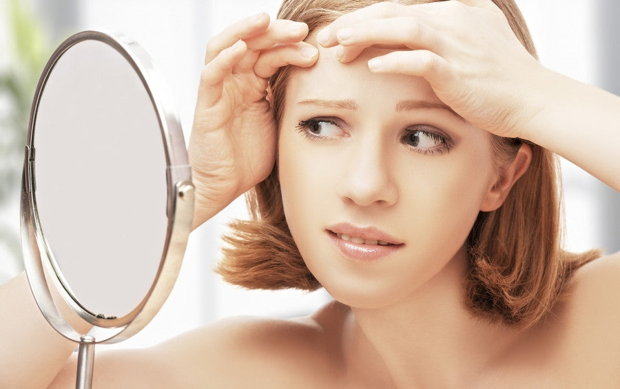 Brush On Block image of woman examining blemish in mirror.