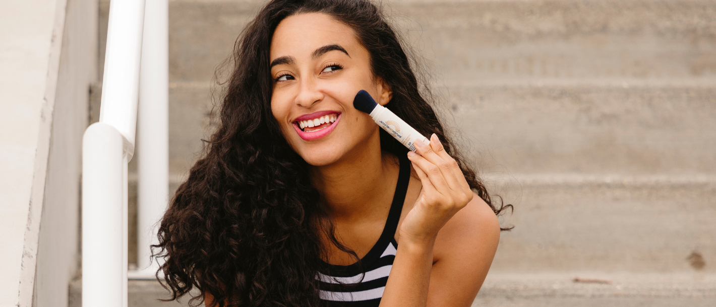 Woman applying Brush On Block mineral powder sunscreen over makeup mid-day without ruining her foundation