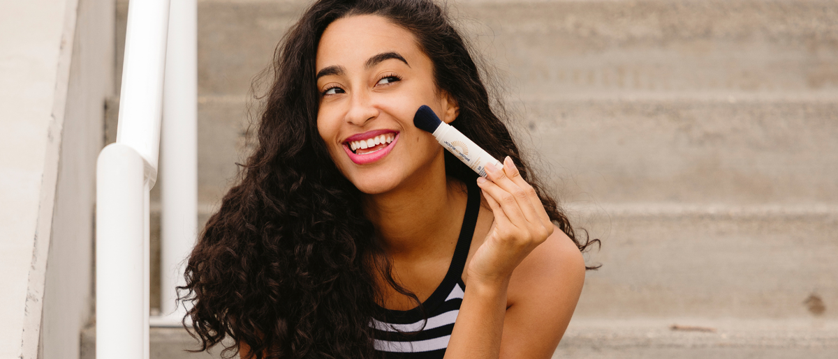 Woman applying Brush On Block mineral powder sunscreen over makeup mid-day without ruining her foundation