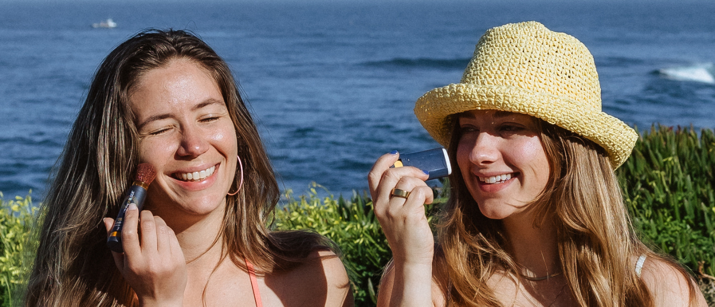 Two women applying mineral sunscreen outside on a summer afternoon