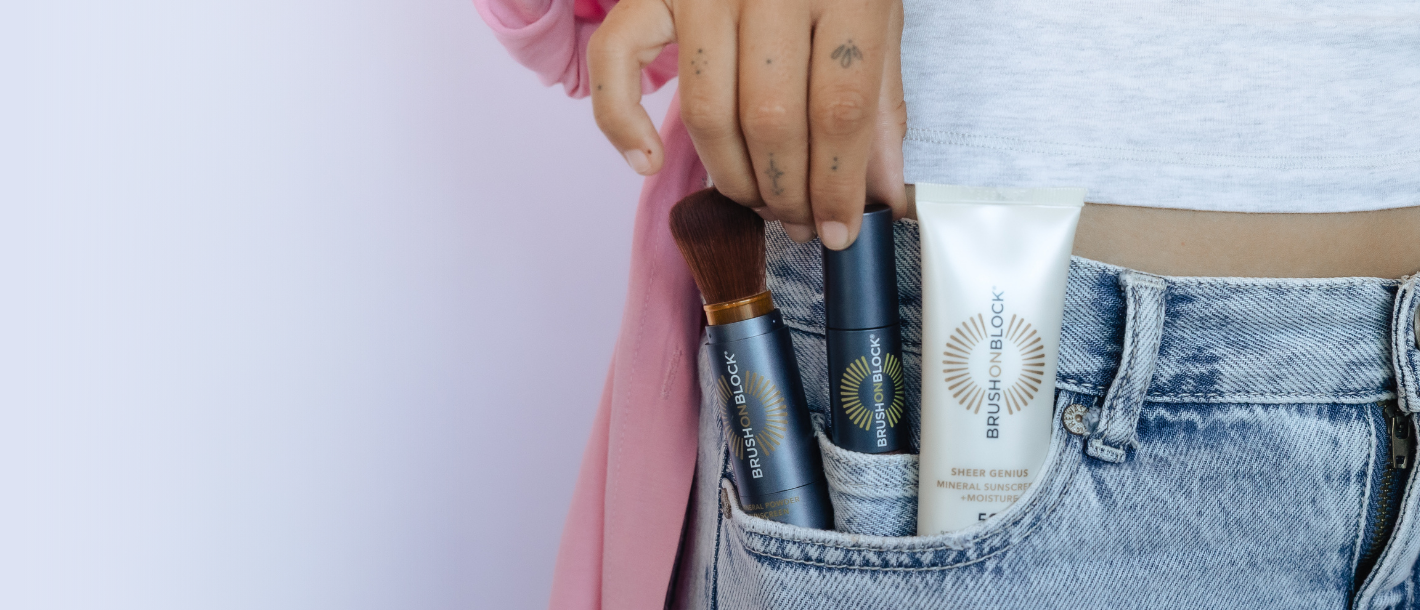 Close-up of a hand pulling two sunscreen brushes and a lotion from a pocket, representing daily, on-the-go sun protection.