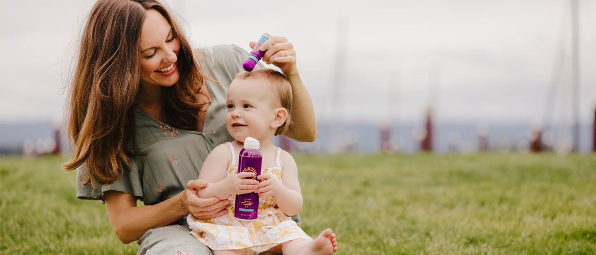 Mother applying Brush On Block BOB KIDS mineral powder sunscreen to her toddler’s scalp as the child sits on her lap