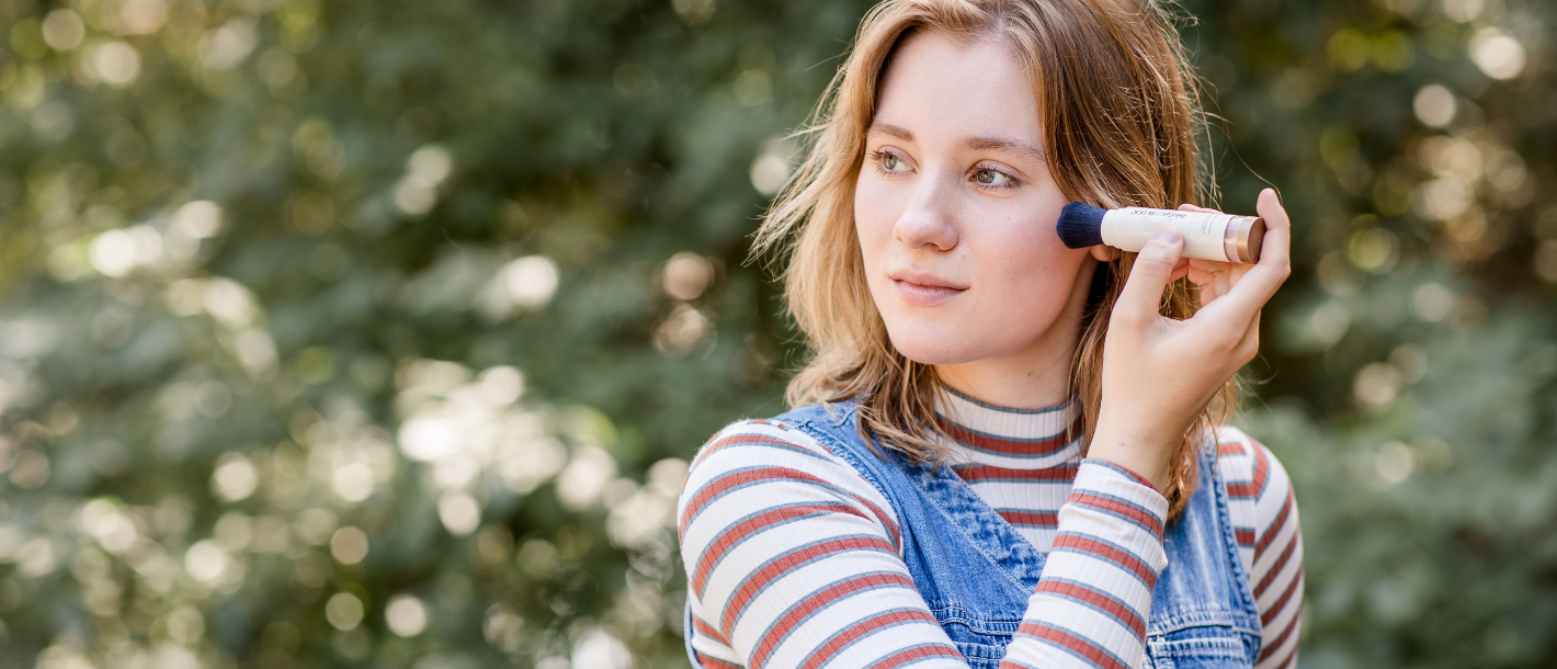 Woman applying Brush On Block mineral powder sunscreen outside..