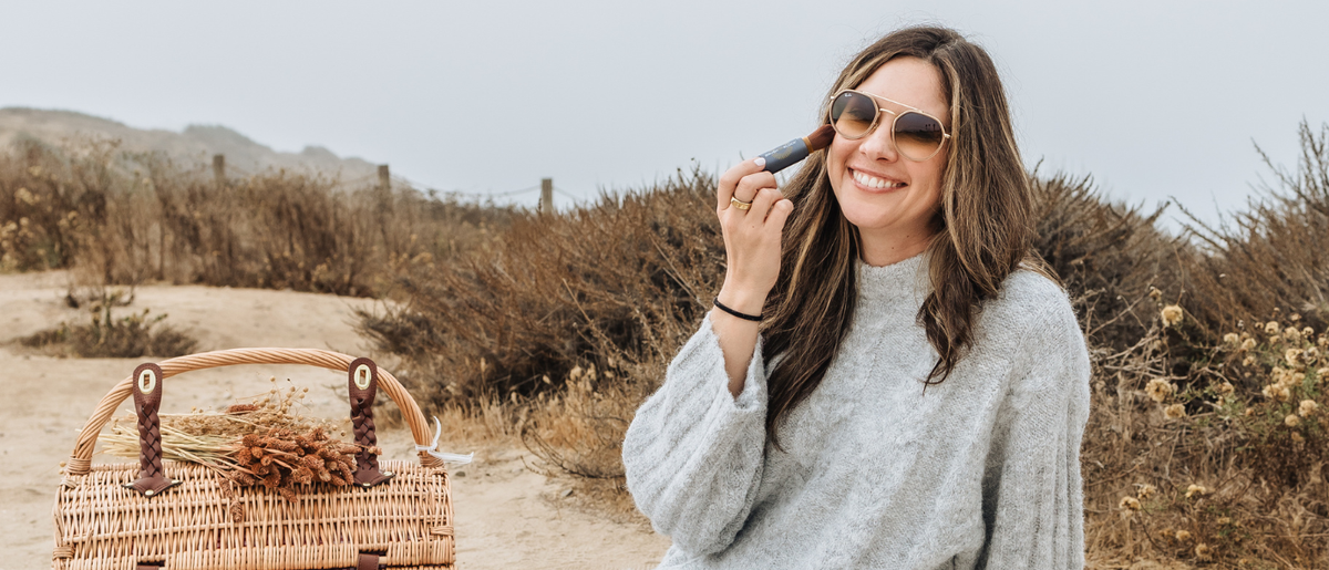 A woman in a fall sweater applying Brush On Block mineral powder sunscreen.