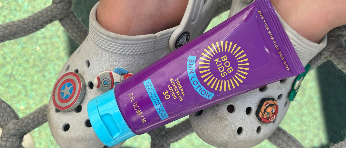BOB KIDS mineral sunscreen lotion resting on children's feet during outdoor play