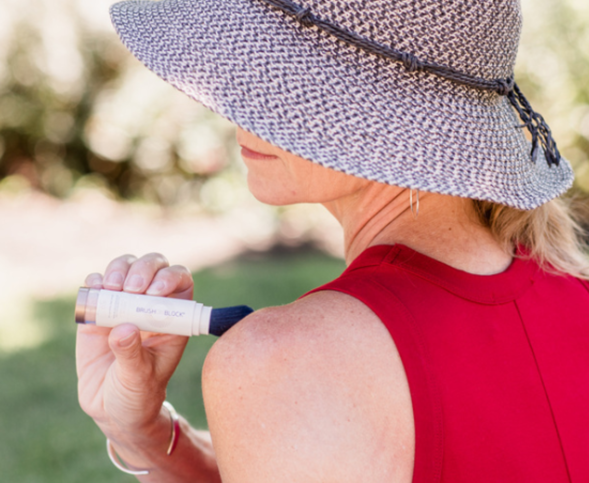 Woman applying Brush On Block SPF 50 to shoulder outdoors
