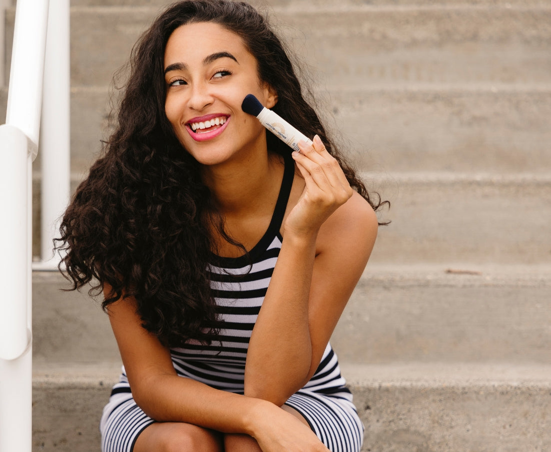 Woman sitting reapplying Brush On Block mineral sunscreen during her day