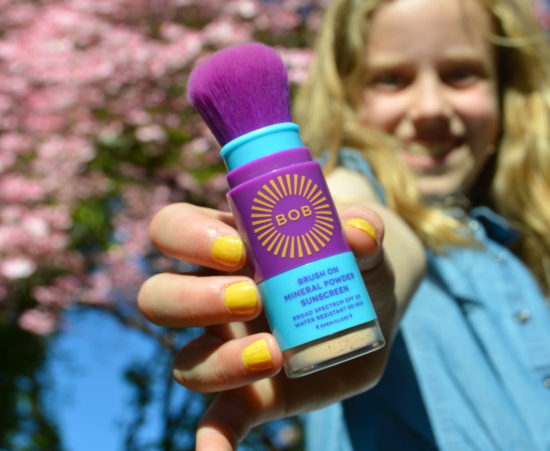 Girl holding a BOB KIDS sunscreen brush.