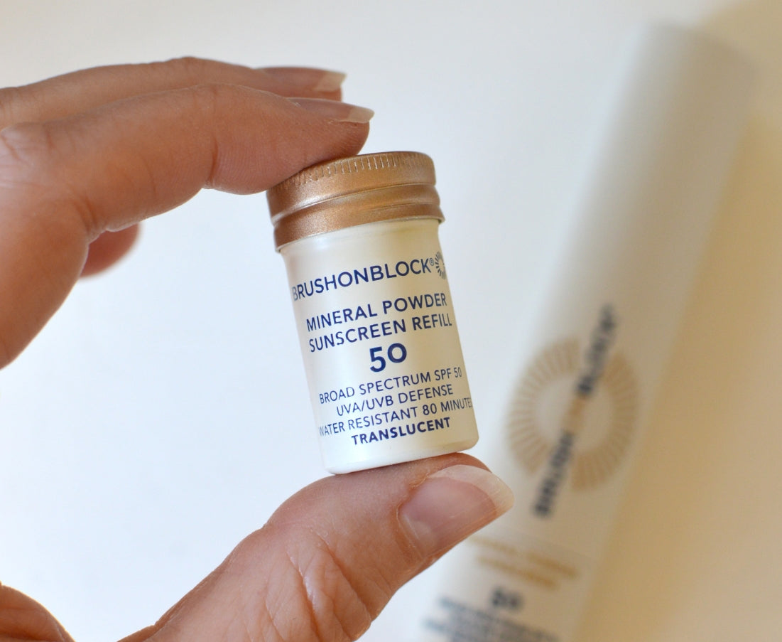 Hand holding a small container of BrushOn Block SPF 50 mineral powder sunscreen refill.