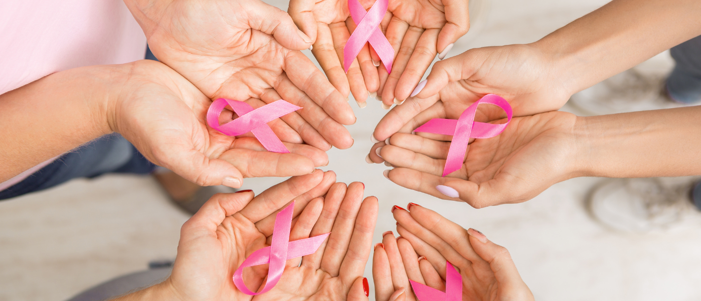 Woman’s hand holding a pink ribbon for breast cancer awareness. 
