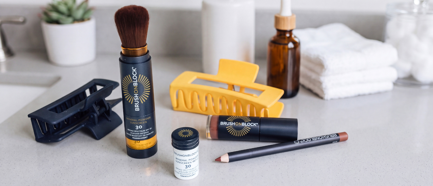 Brush On Block SPF 30 Mineral Powder Sunscreen brush with the cap off, standing on a bathroom counter in daylight beside skincare bottles.