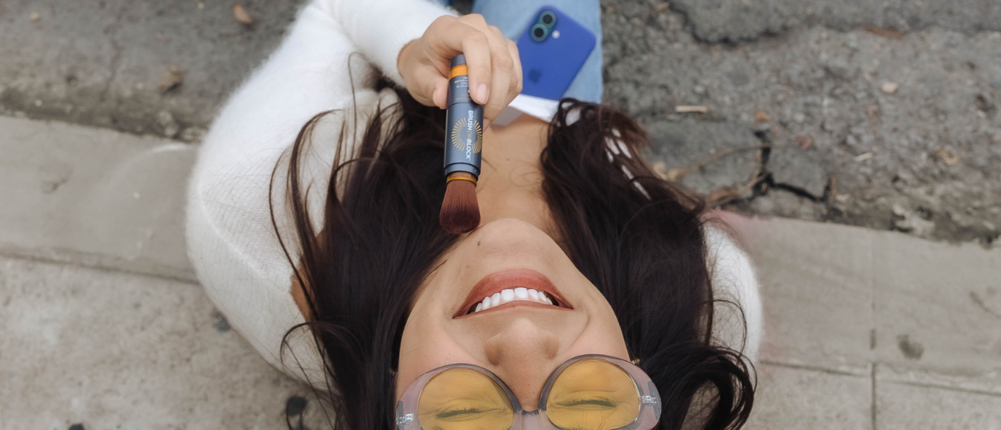 Woman applying Brush On Block mineral powder sunscreen outdoors in natural light
