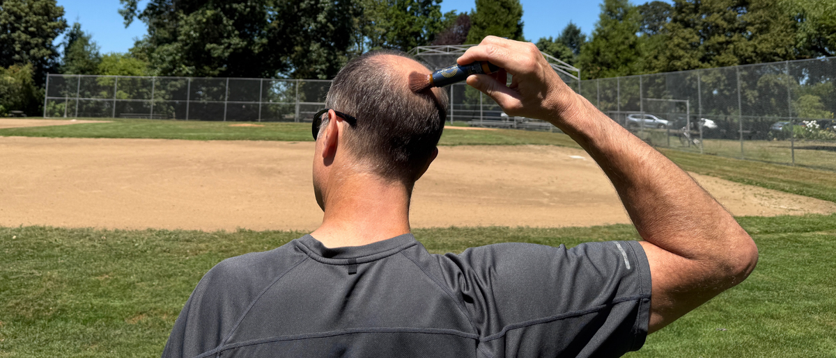 Man applying Brush On Block mineral powder sunscreen to his bald scalp outdoors using the built-in brush applicator.