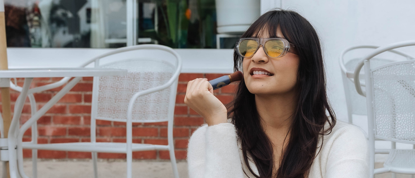 Woman applying Brush On Block mineral powder sunscreen outside without disrupting her makeup or routine. 
