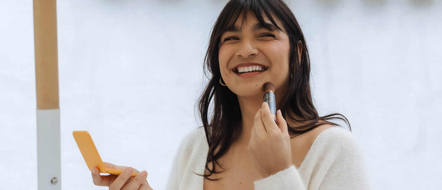Woman applying Brush On Block mineral powder sunscreen for easy, everyday sun protection and reapplication.