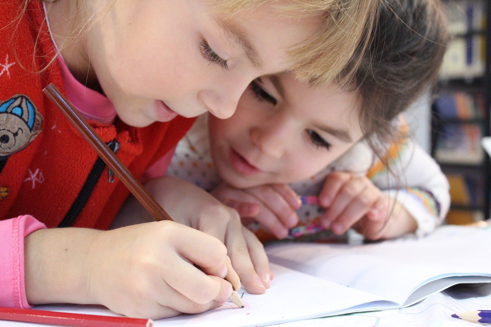 Image of young girl writing in notebook as her friend looks on.