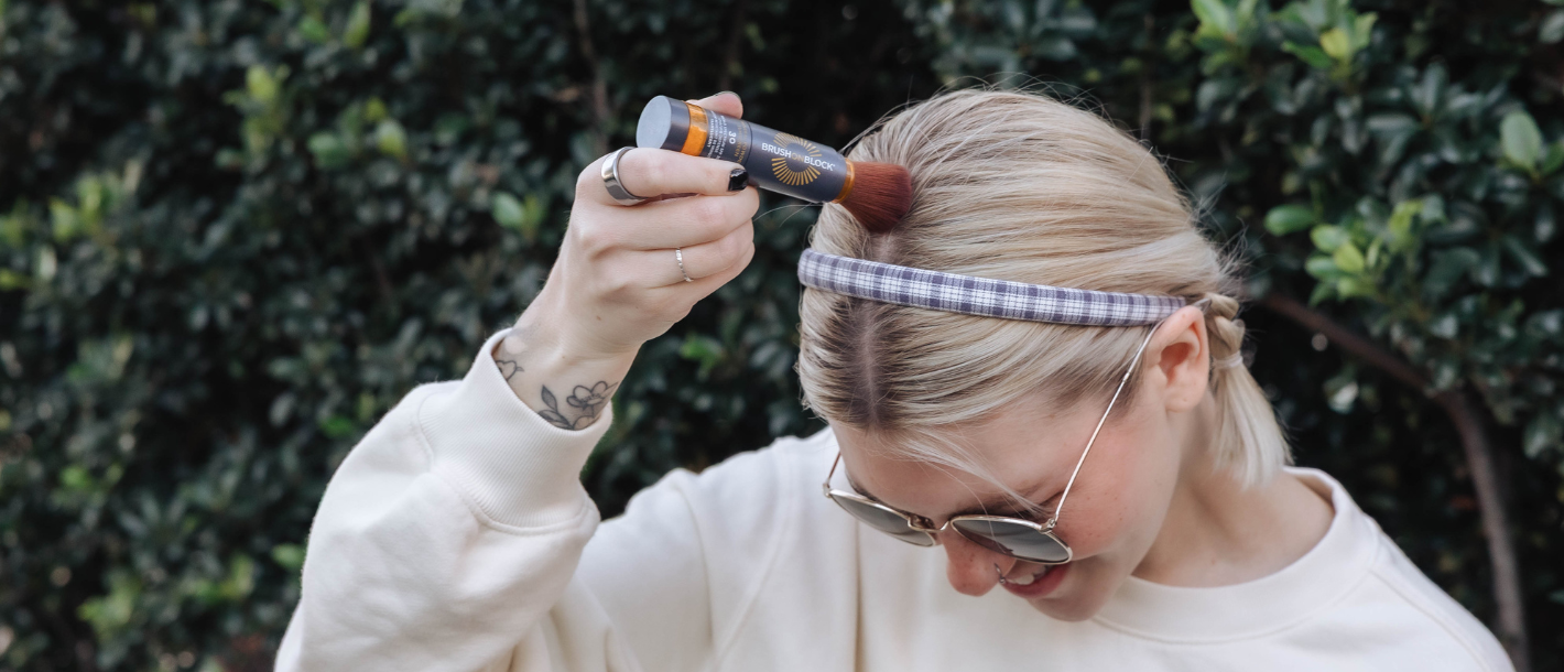 Woman applying mineral powder sunscreen to her scalp along her hair part with a Brush On Block brush.