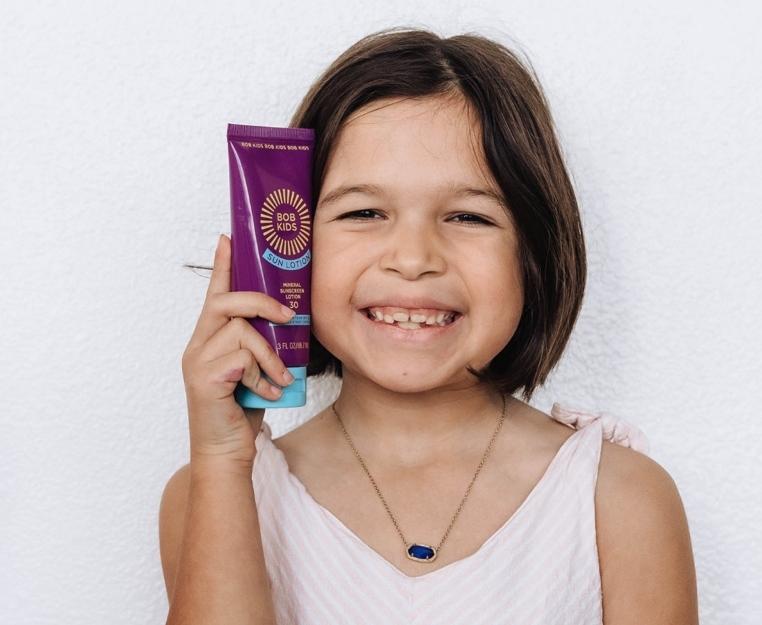 Young girl holding a purple tube of BOB KIDS SPF 30 Mineral Sun Lotion