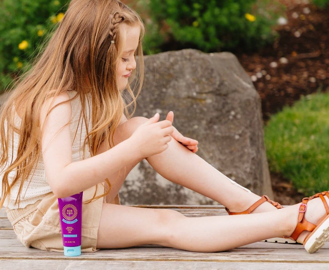Young girl sitting on a bench applying BOB KIDS SPF 30 Mineral Sun Lotion