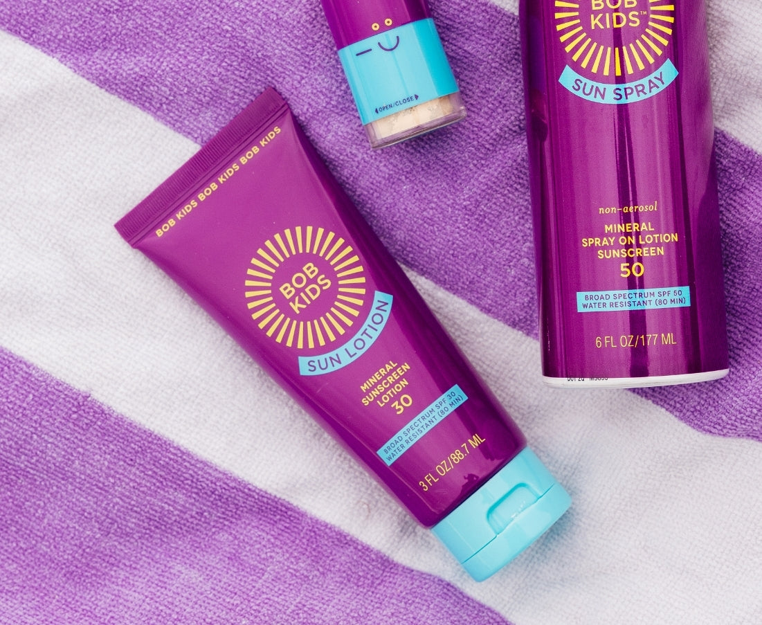 BOB KIDS lotion, spray and mineral powder lying on a beach towel. 