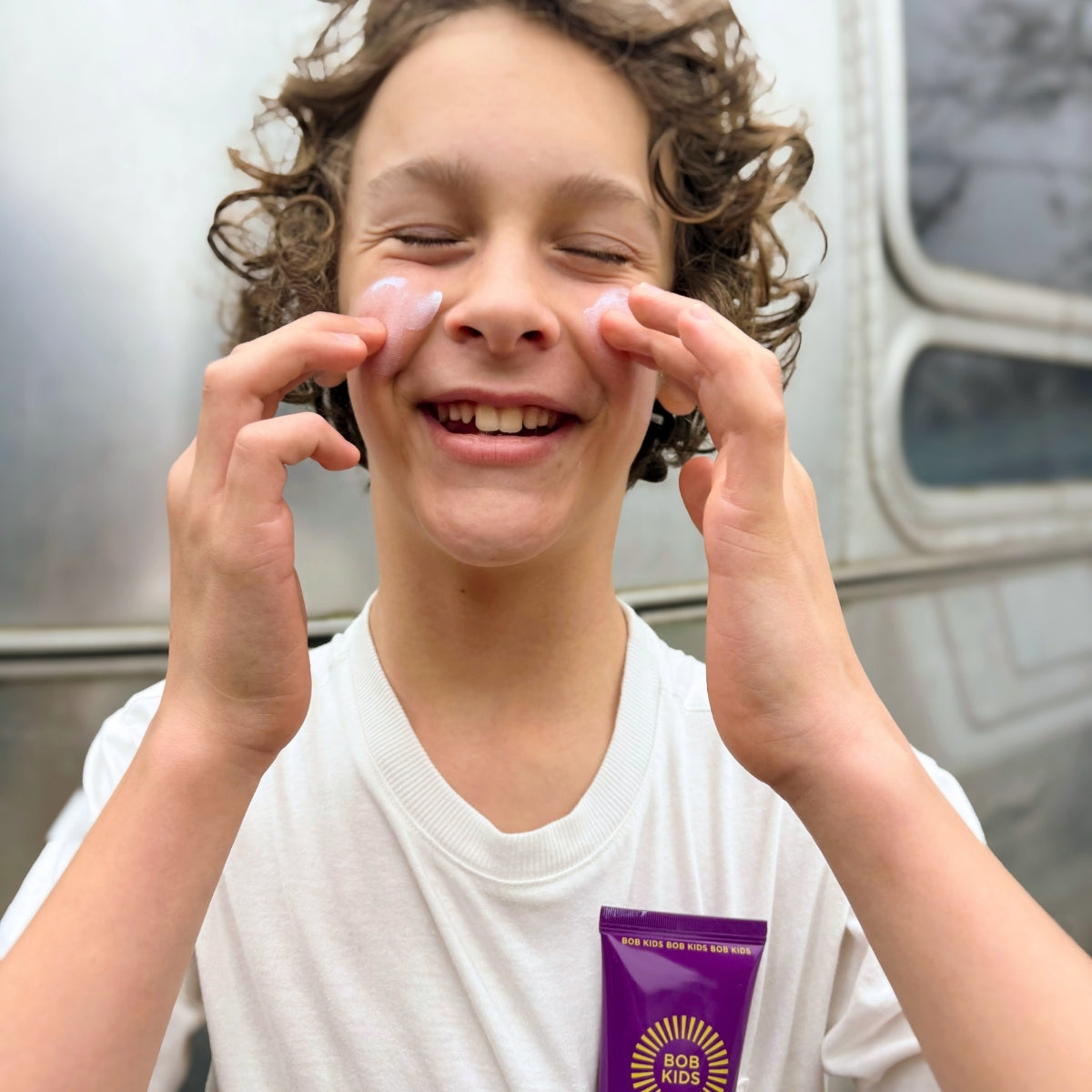 Young boy applying BOB KIDS SPF 30 Mineral Sun Lotion to his face 