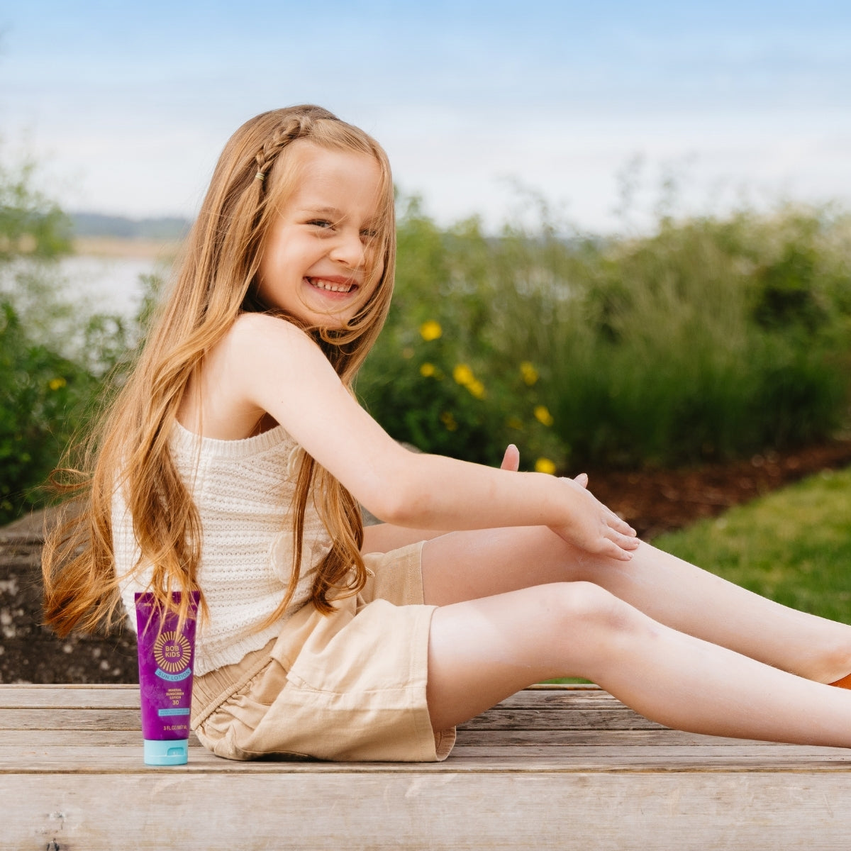 Young girl sitting on a bench applying BOB KIDS SPF 30 Mineral Sun Lotion