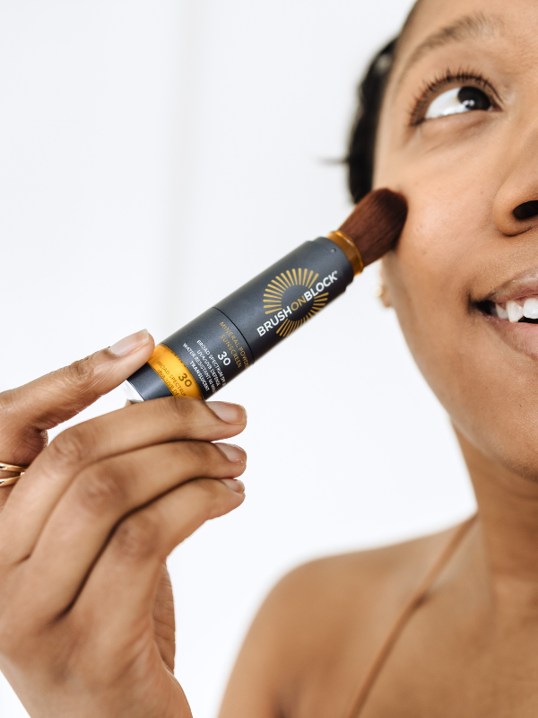 Woman applying Brush On Block SPF 30 translucent mineral powder sunscreen to her cheek 