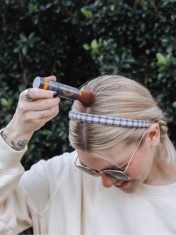 Woman applying Brush On Block SPF 30 Mineral Powder Sunscreen to her hair part 