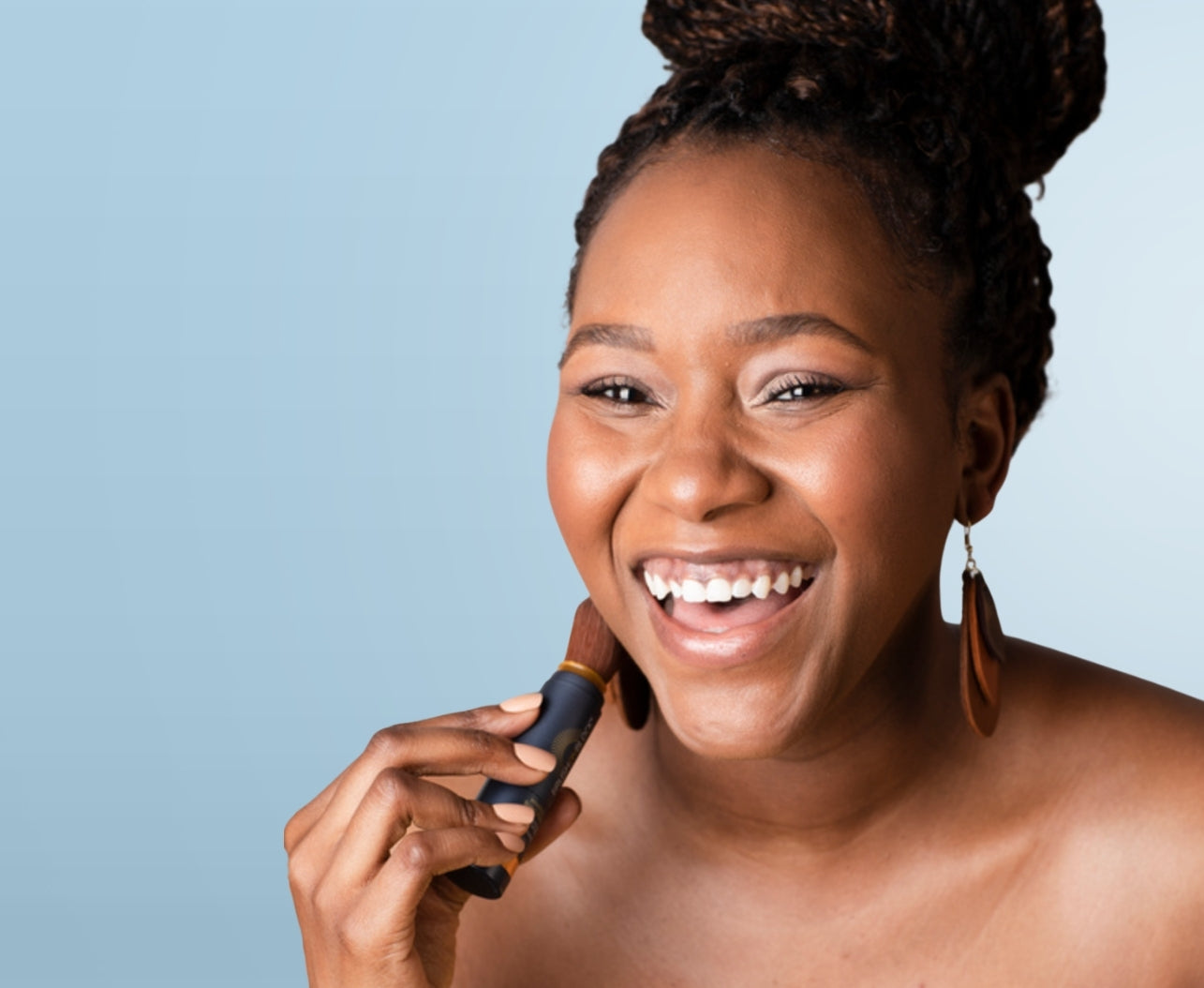 Woman with a dark skin tone applying Brush On Block Translucent Mineral Powder Sunscreen, showing invisible coverage with no white cast.