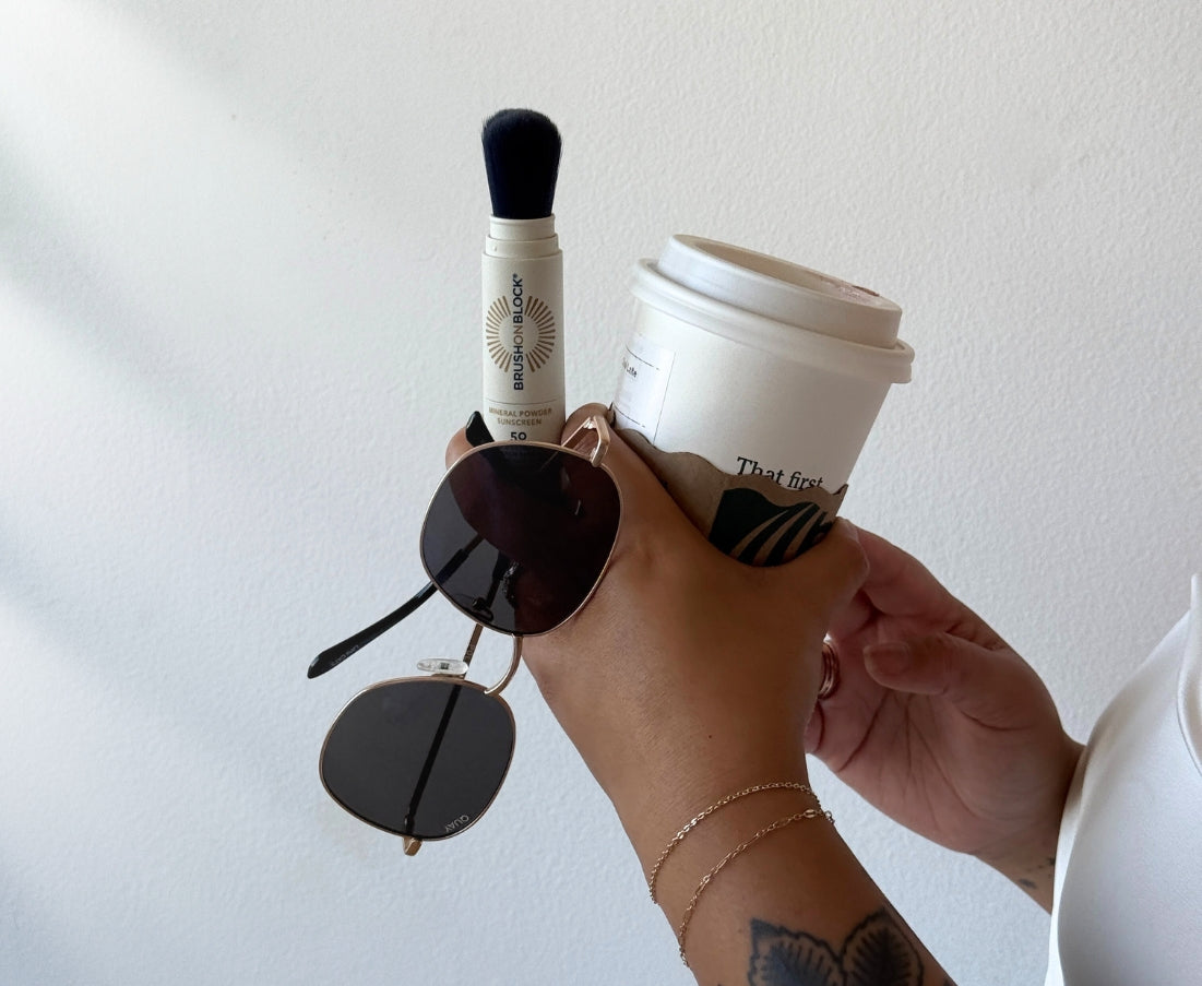 Hand holding a coffee cup, Brush On Block and sunglasses, showing easy on the go application