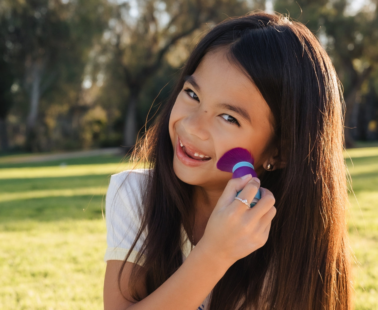 Young girl applying Brush-On-Block Mineral Power Sunscreen to her cheek at the park 