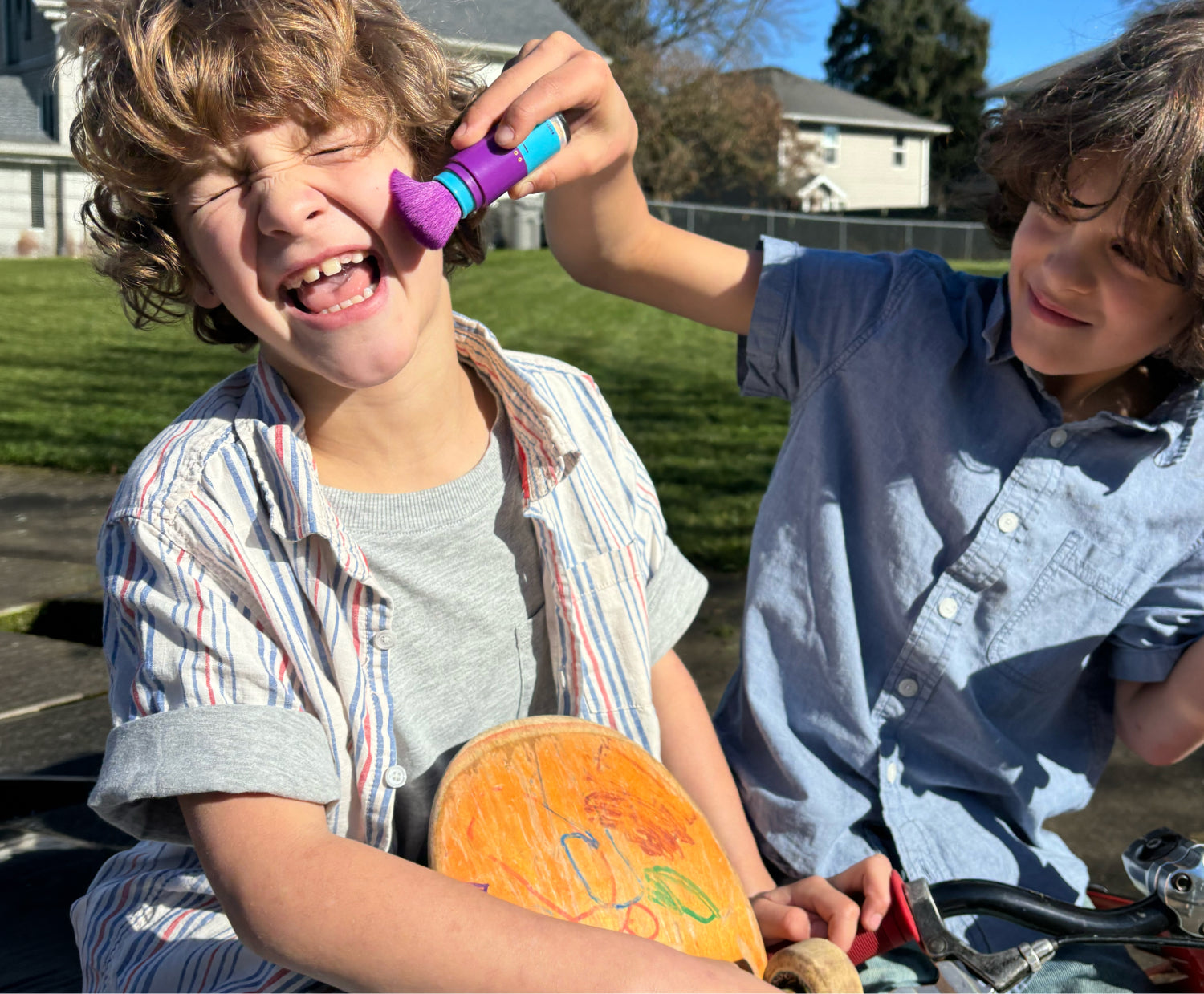 Two children playing outdoors on a sunny day with one applying Brush-On-Block to the other's cheek.