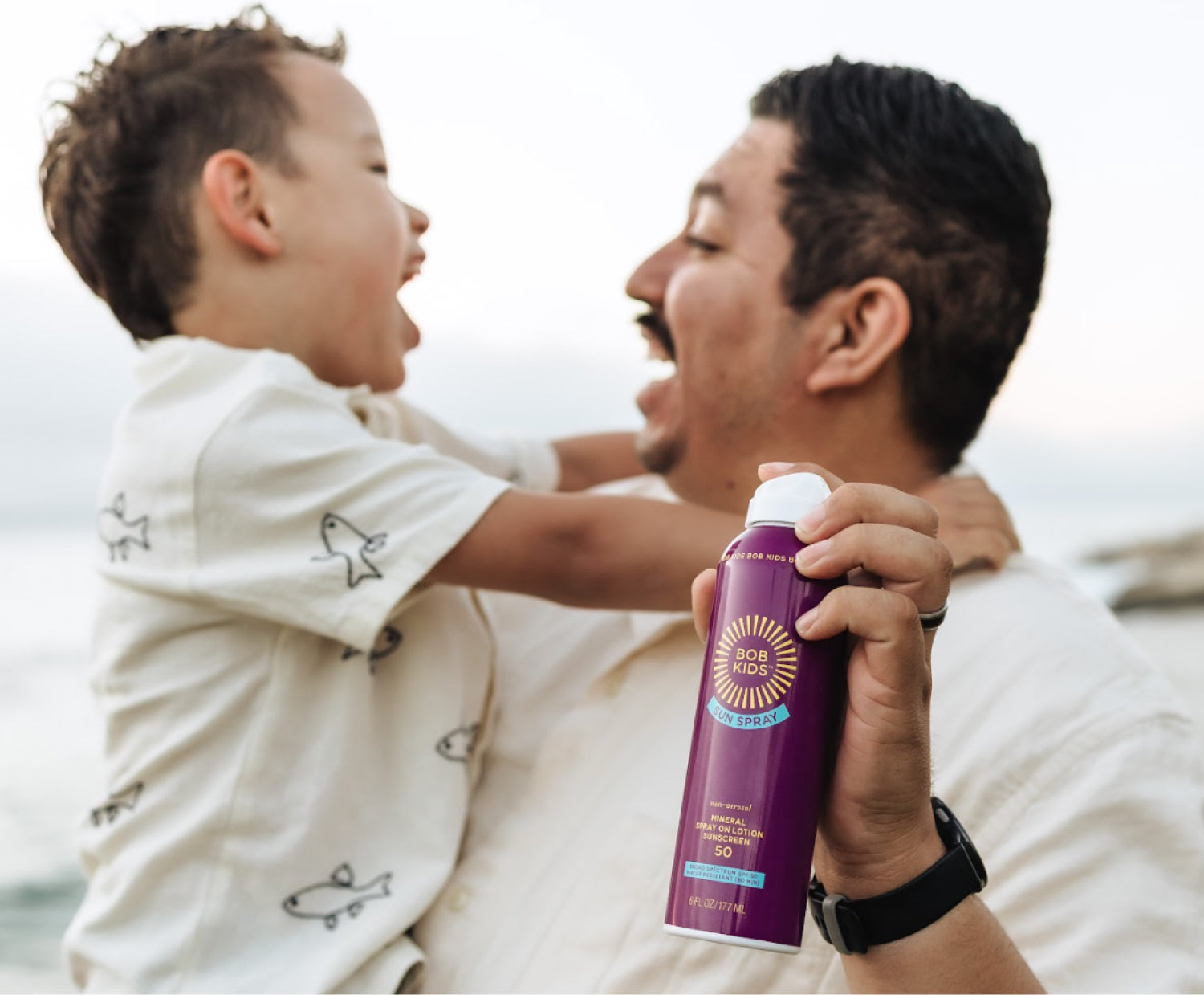 Man holding a child with BOB KIDS Mineral Sun Spray in hand