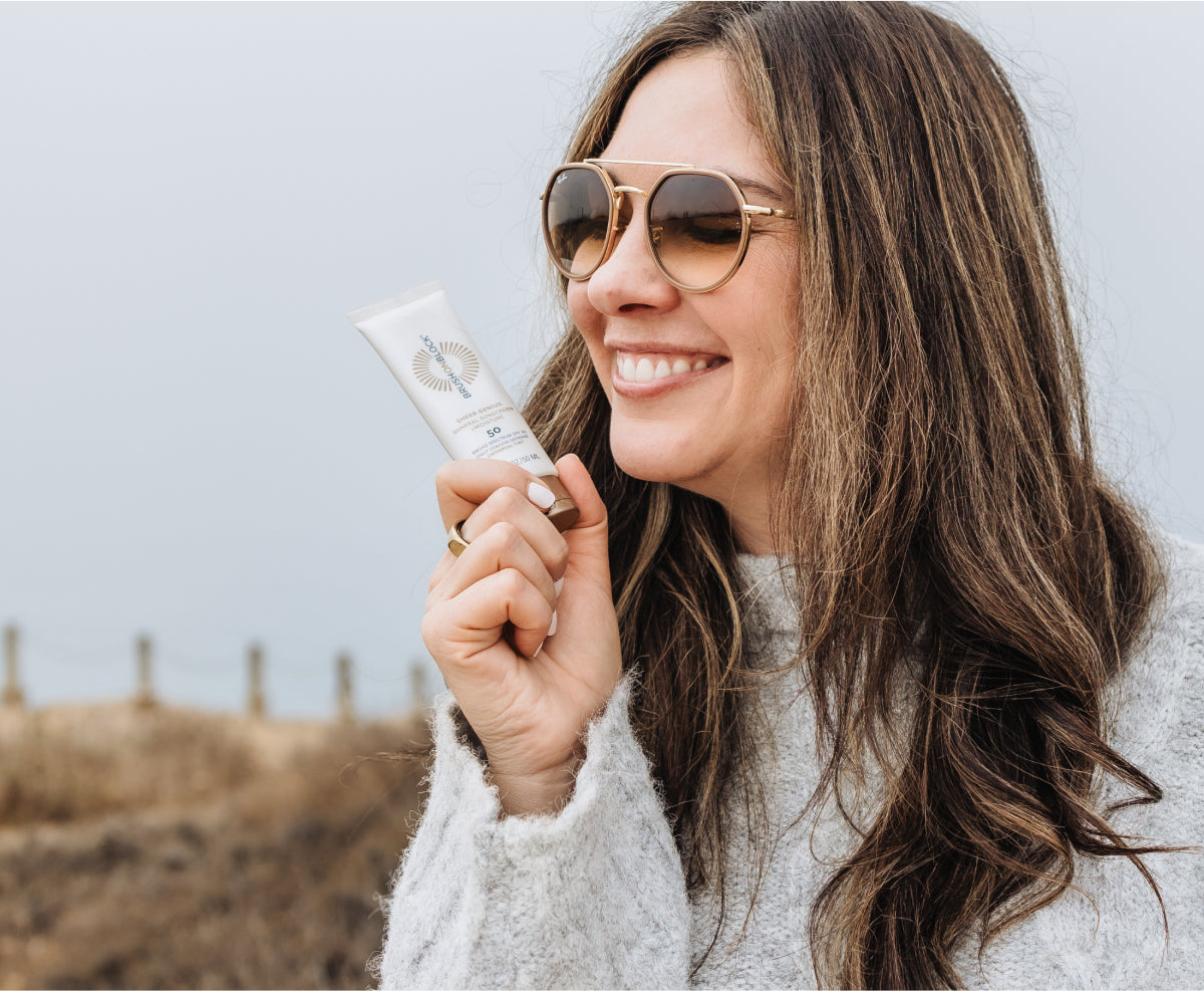 Woman holding Sheer Genius SPF 50 mineral sunscreen lotion with moisture.