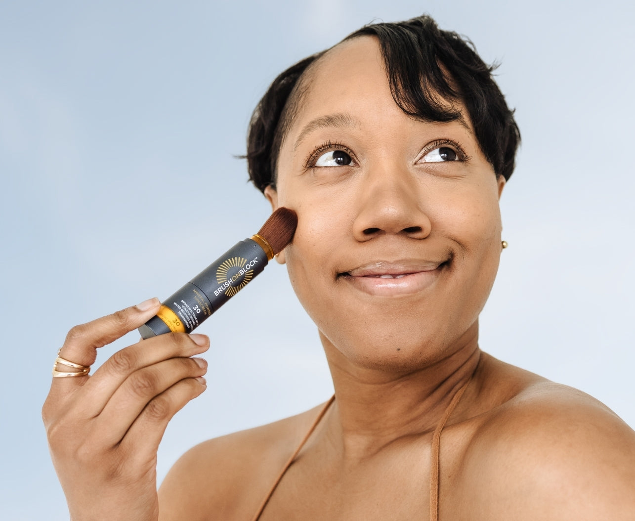Woman applying Brush On Block mineral powder sunscreen that absorbs excess oil, controls shine, and leaves skin with a clean, matte finish.