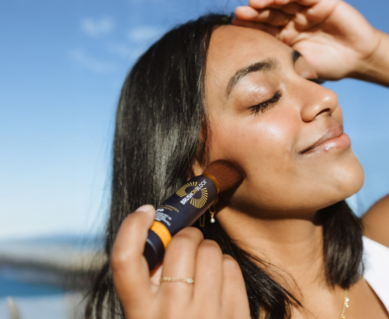 Woman applying Brush On Block mineral powder sunscreen to her cheek, demonstrating breathable, non-comedogenic coverage with a natural look.