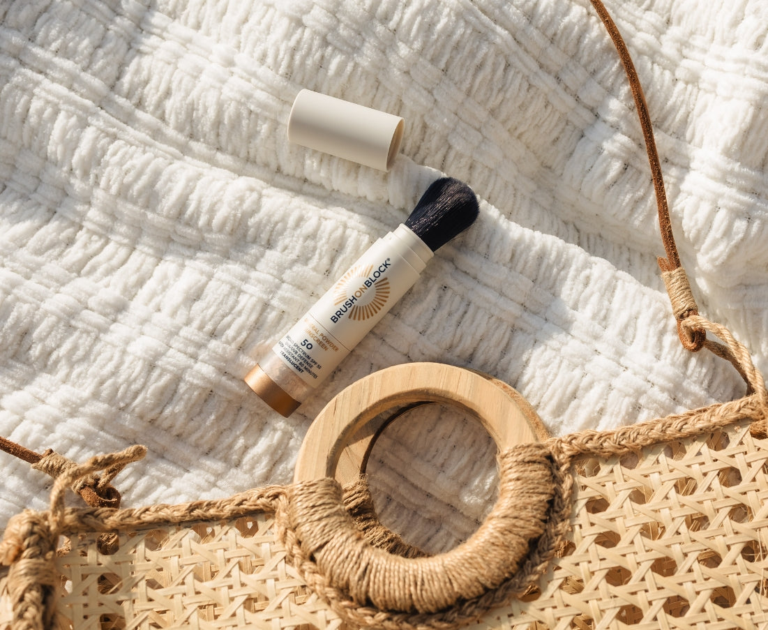 Brush On Block SPF 50 brush with cap off on blanket next to handbag