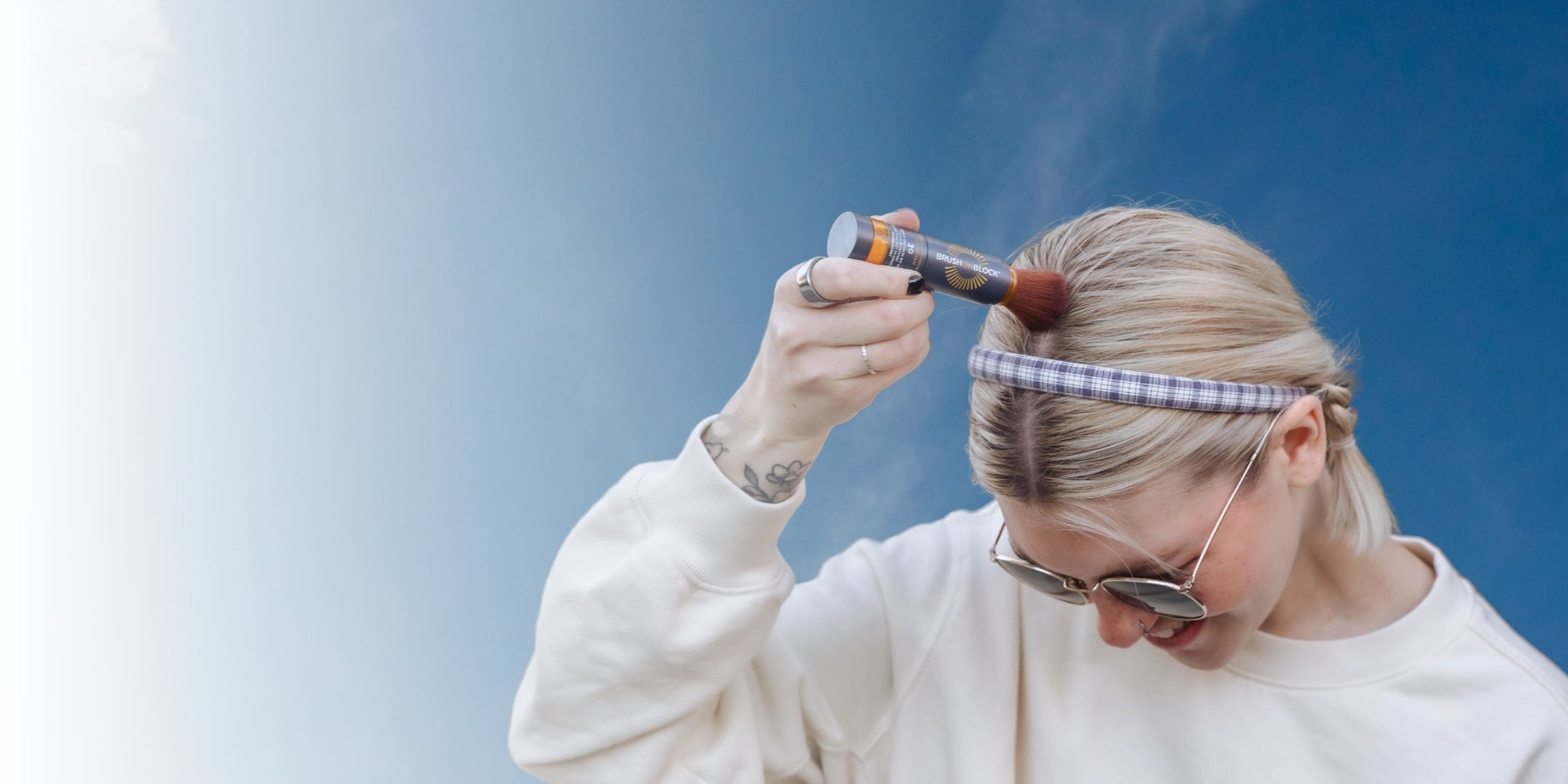Woman applying mineral powder sunscreen to her scalp along her hair part using a Brush On Block brush.