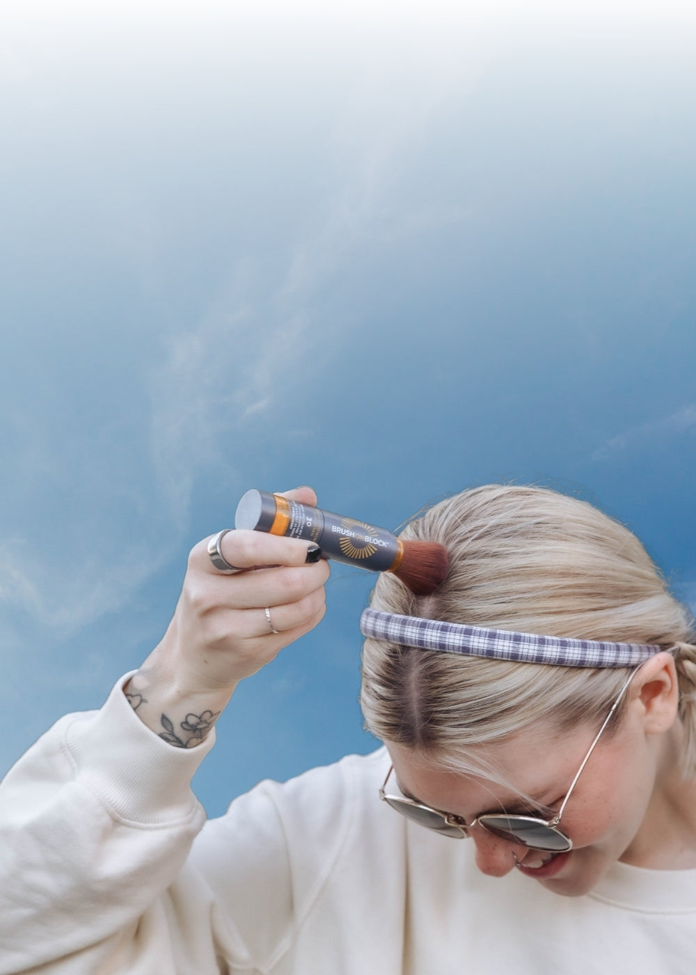 Woman applying mineral powder sunscreen to her scalp along her hair part using a Brush On Block brush.