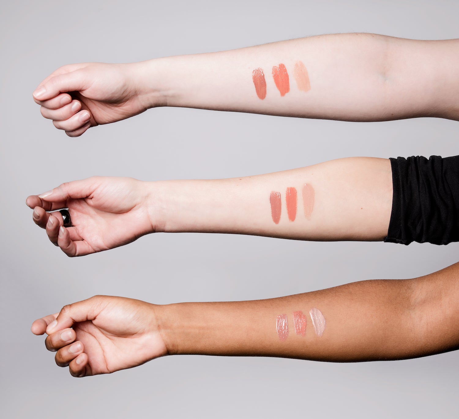 Three arms of varying skin tones with Fig, Coral and Nude Tint BRUSH ON BLOCK® Protective Lip Oil swatched on them.