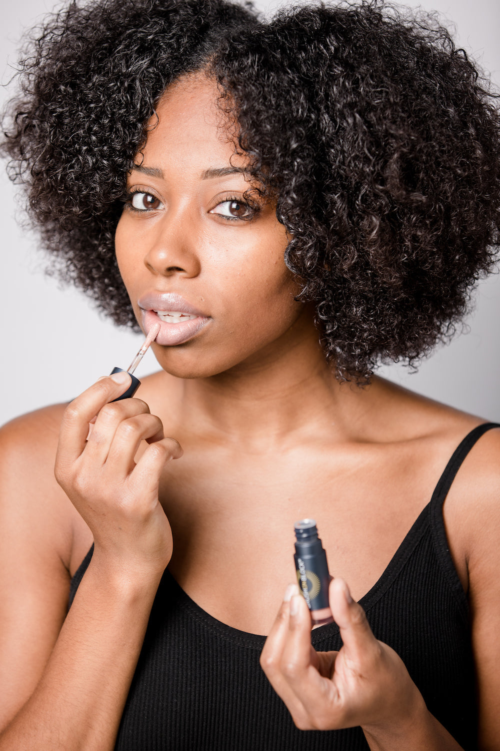 Deep skin tone, brunette woman applying BRUSH ON BLOCK® Protective Lip Oil SPF 32 Nude Tint